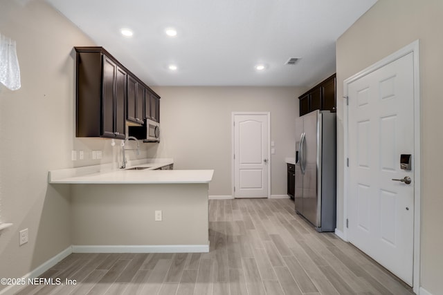 kitchen with appliances with stainless steel finishes, sink, kitchen peninsula, dark brown cabinets, and light wood-type flooring