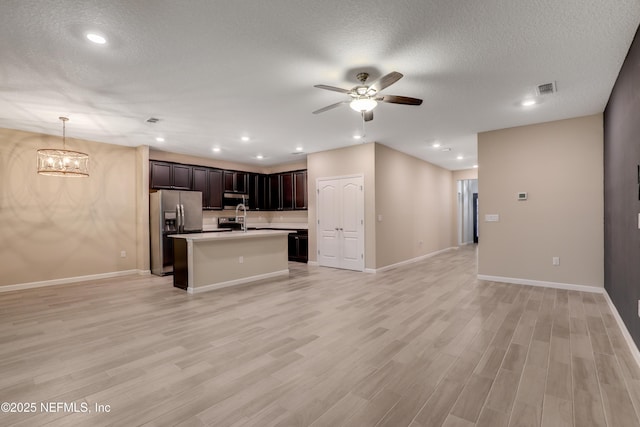 kitchen with ceiling fan with notable chandelier, pendant lighting, an island with sink, stainless steel refrigerator with ice dispenser, and light wood-type flooring