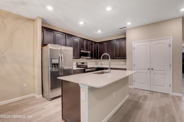 kitchen featuring sink, dark brown cabinets, stainless steel appliances, light hardwood / wood-style floors, and an island with sink