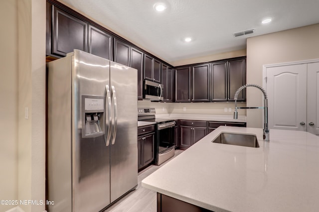 kitchen with dark brown cabinetry, sink, a center island with sink, and appliances with stainless steel finishes