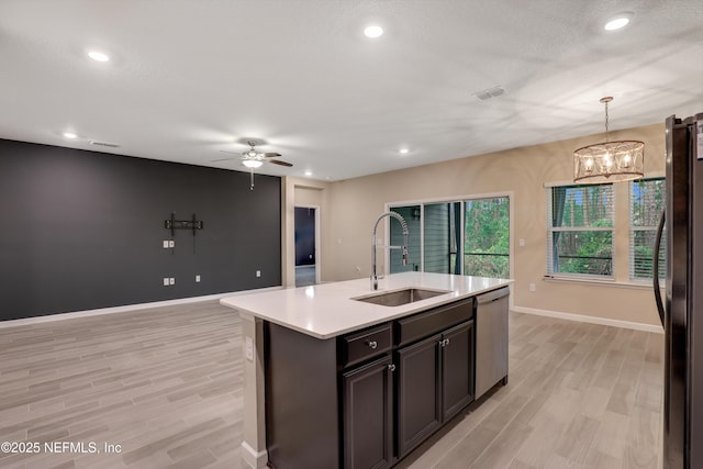 kitchen featuring pendant lighting, sink, stainless steel dishwasher, black fridge, and a center island with sink