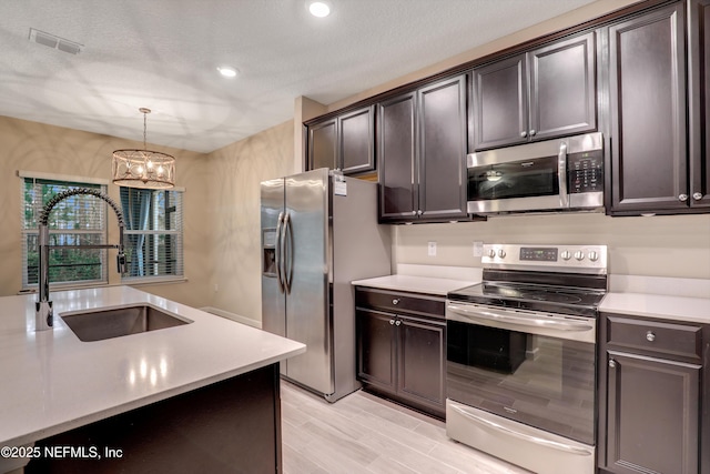 kitchen featuring pendant lighting, sink, stainless steel appliances, dark brown cabinets, and a textured ceiling