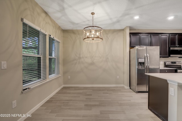 kitchen featuring appliances with stainless steel finishes, hanging light fixtures, a notable chandelier, dark brown cabinetry, and light hardwood / wood-style floors