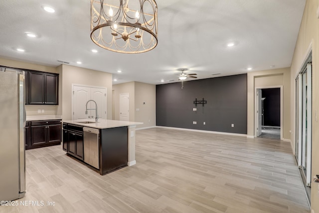 kitchen with stainless steel appliances, sink, light hardwood / wood-style floors, and a kitchen island with sink