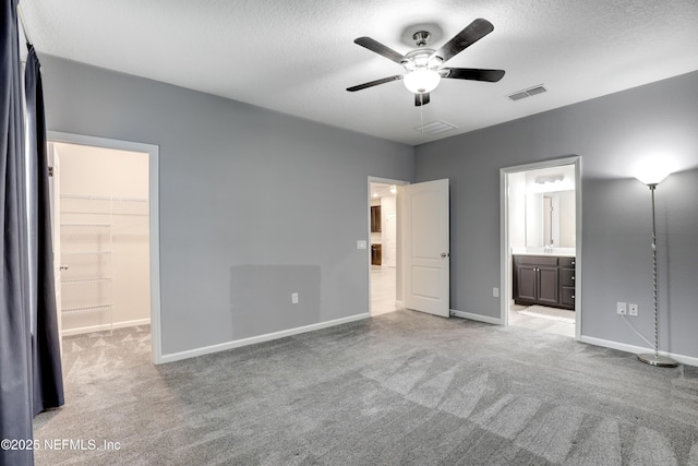 unfurnished bedroom featuring light carpet, a walk in closet, a textured ceiling, and ensuite bathroom