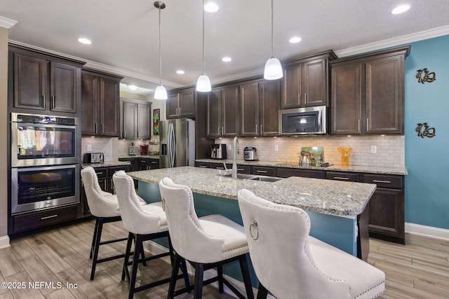 kitchen with stainless steel appliances, an island with sink, a sink, and pendant lighting