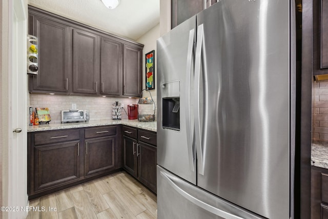 kitchen featuring dark brown cabinetry, light stone countertops, stainless steel fridge, and backsplash