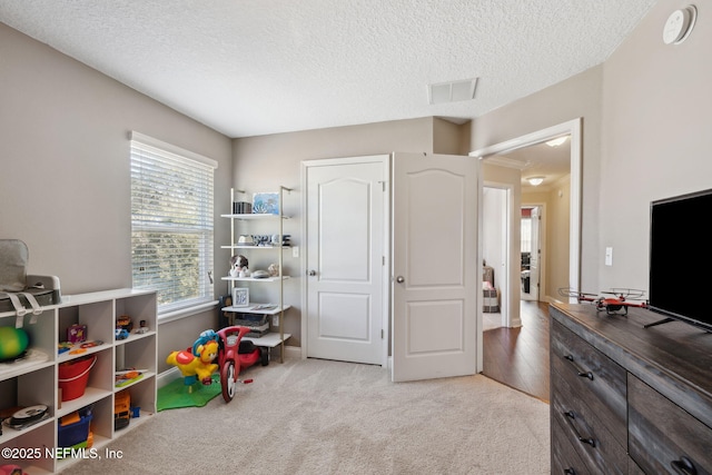 rec room featuring light colored carpet, visible vents, and a textured ceiling