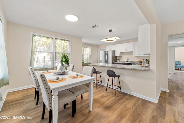 dining room featuring light wood finished floors, visible vents, and baseboards