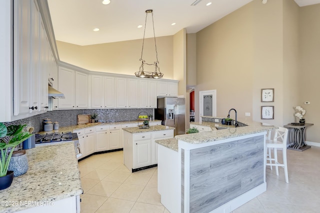 kitchen with stainless steel fridge, hanging light fixtures, light stone counters, white cabinets, and a kitchen island