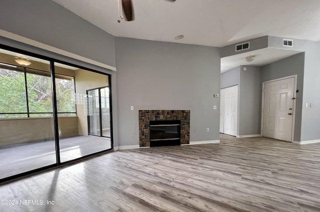 unfurnished living room with ceiling fan, lofted ceiling, a tiled fireplace, and light hardwood / wood-style flooring