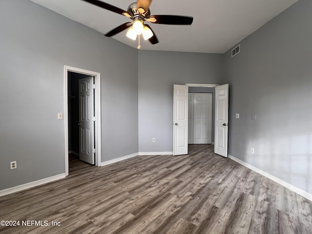 unfurnished bedroom featuring ceiling fan, a walk in closet, wood-type flooring, and a closet