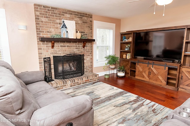 living room featuring hardwood / wood-style flooring, ceiling fan, and a brick fireplace