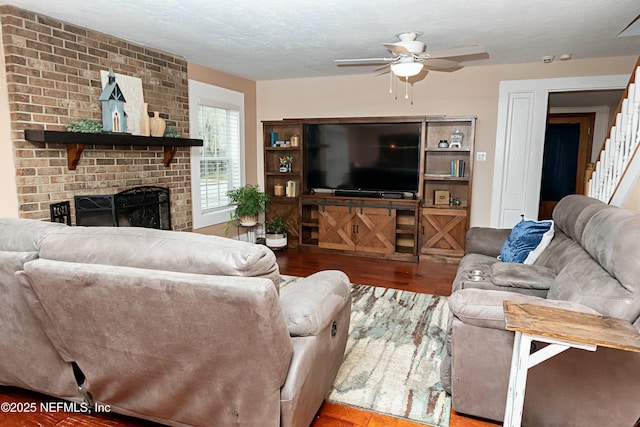 living room featuring ceiling fan, a brick fireplace, hardwood / wood-style floors, and a textured ceiling