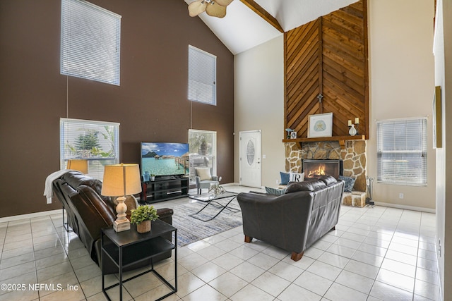 living area with ceiling fan, light tile patterned flooring, baseboards, and a stone fireplace