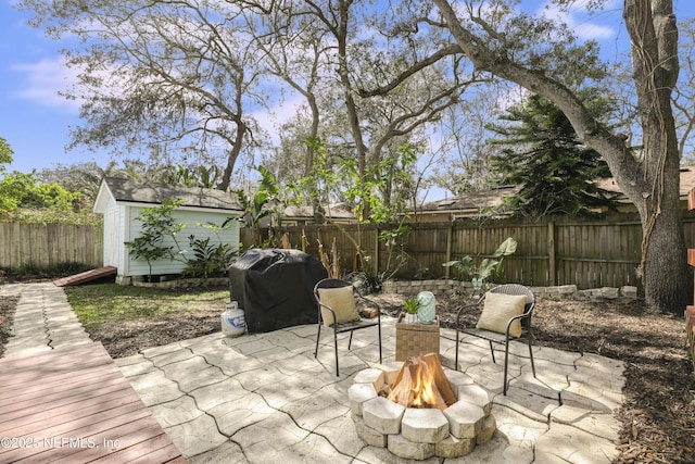 view of patio with a storage shed, a fire pit, area for grilling, a fenced backyard, and an outdoor structure