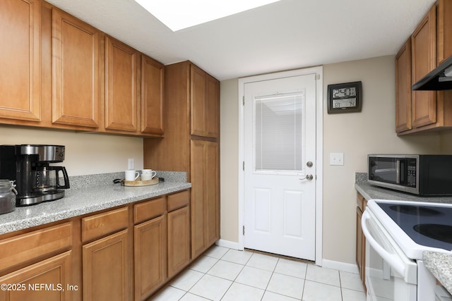 kitchen with light tile patterned floors, light countertops, white range with electric stovetop, brown cabinets, and stainless steel microwave