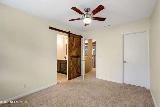 unfurnished bedroom featuring light carpet, a barn door, visible vents, and baseboards