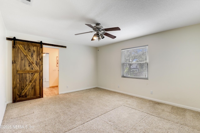 unfurnished room with carpet floors, a barn door, ceiling fan, a textured ceiling, and baseboards