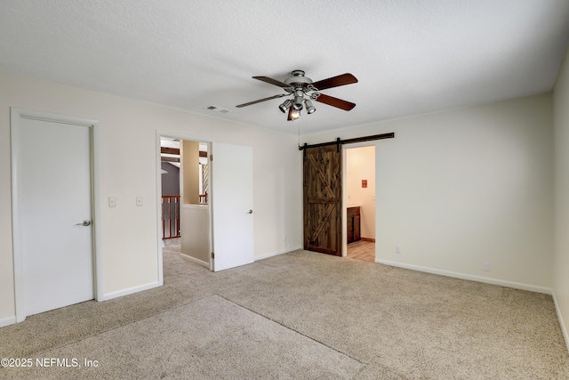 unfurnished bedroom with a barn door, baseboards, visible vents, a textured ceiling, and carpet flooring