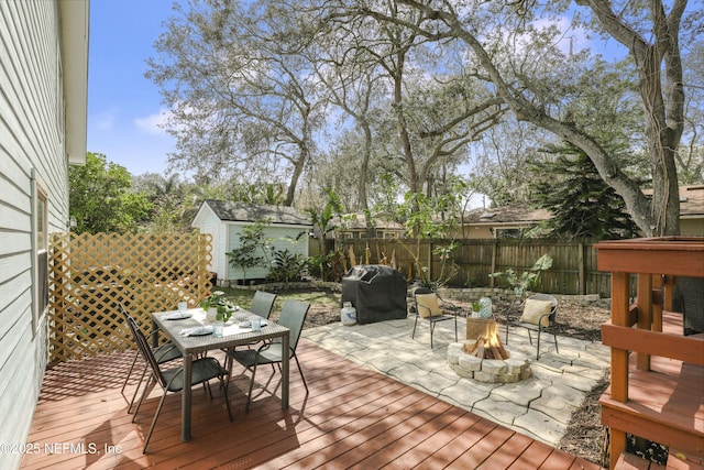 wooden terrace featuring outdoor dining area, area for grilling, an outdoor fire pit, fence, and an outdoor structure