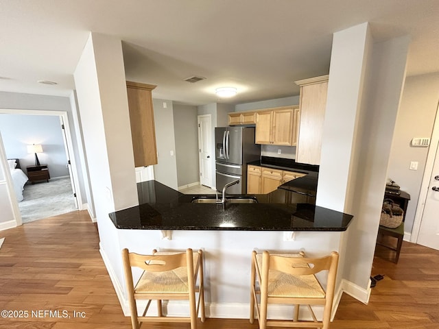 kitchen with a kitchen bar, light brown cabinetry, sink, stainless steel fridge, and kitchen peninsula