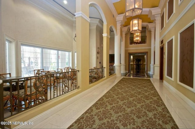 hallway featuring crown molding, tile patterned flooring, decorative columns, and a high ceiling
