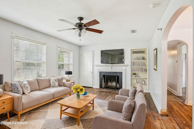 living room with a brick fireplace, ceiling fan, and wood-type flooring