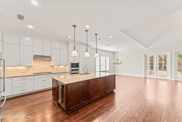 kitchen featuring appliances with stainless steel finishes, pendant lighting, an island with sink, white cabinets, and light stone countertops