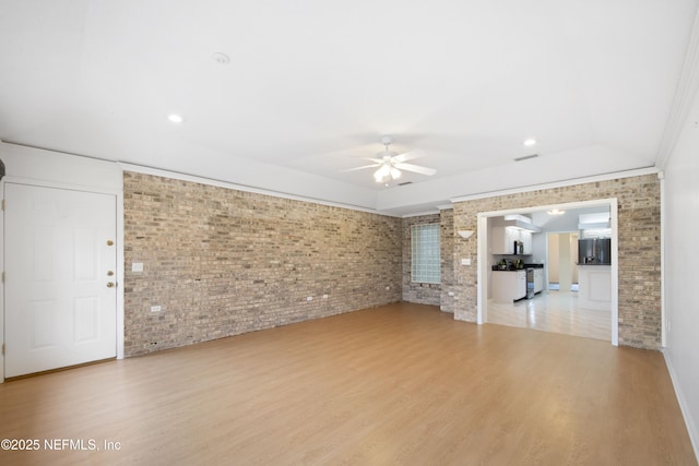 unfurnished living room featuring ceiling fan, brick wall, and light hardwood / wood-style floors