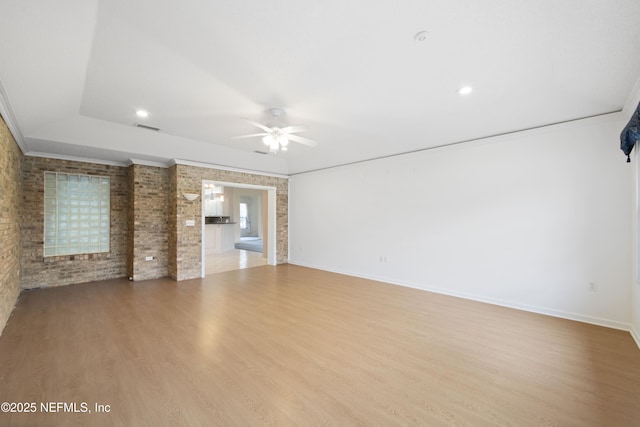 unfurnished room with crown molding, ceiling fan, brick wall, and light hardwood / wood-style flooring