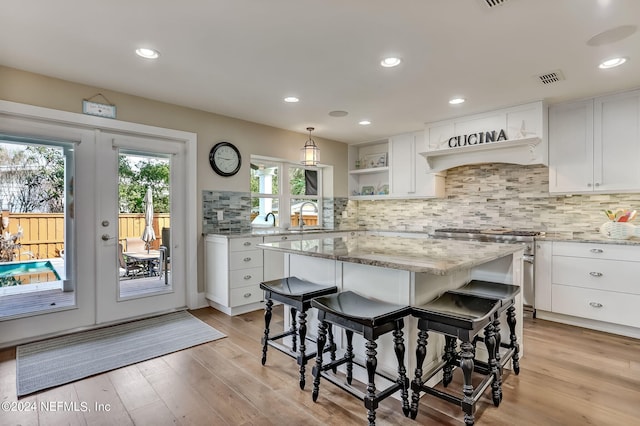 kitchen with light stone counters, stainless steel range, a kitchen island, white cabinets, and french doors