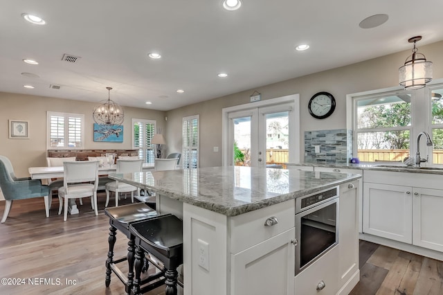 kitchen featuring sink, white cabinetry, light stone counters, and decorative light fixtures