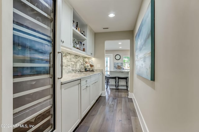 bar with sink, beverage cooler, white cabinetry, light stone countertops, and tasteful backsplash