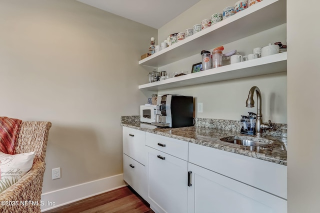 bar featuring dark wood-type flooring, sink, light stone counters, and white cabinets