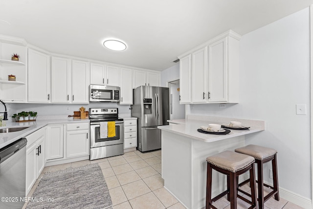 kitchen with sink, white cabinets, a kitchen bar, light tile patterned floors, and stainless steel appliances