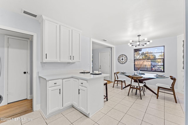 kitchen featuring light tile patterned flooring, white cabinets, an inviting chandelier, and kitchen peninsula