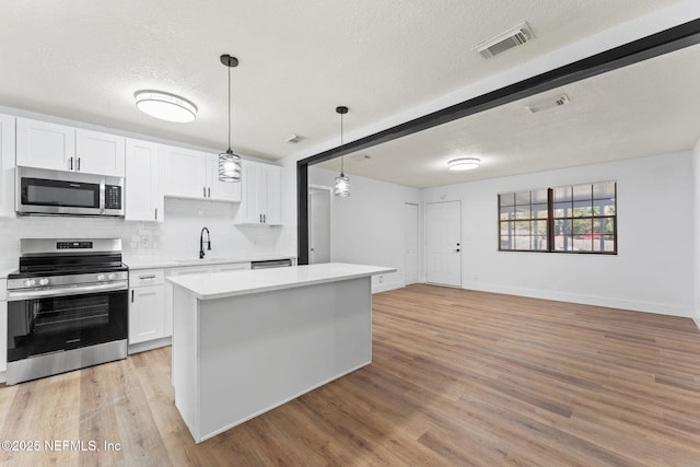 kitchen with appliances with stainless steel finishes, decorative light fixtures, tasteful backsplash, white cabinets, and a center island