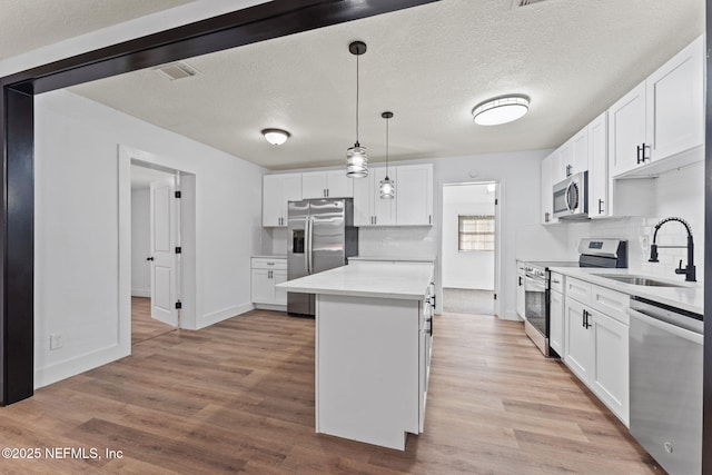 kitchen featuring appliances with stainless steel finishes, decorative light fixtures, sink, white cabinets, and light wood-type flooring