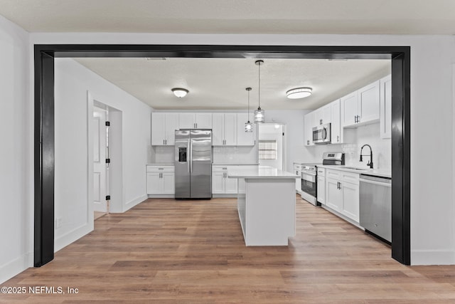 kitchen featuring pendant lighting, stainless steel appliances, white cabinets, and light wood-type flooring