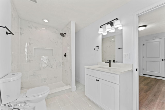 bathroom with vanity, a textured ceiling, toilet, and a tile shower