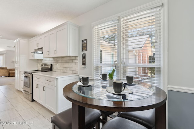 kitchen with white cabinets, stainless steel range with electric stovetop, light tile patterned floors, and tasteful backsplash