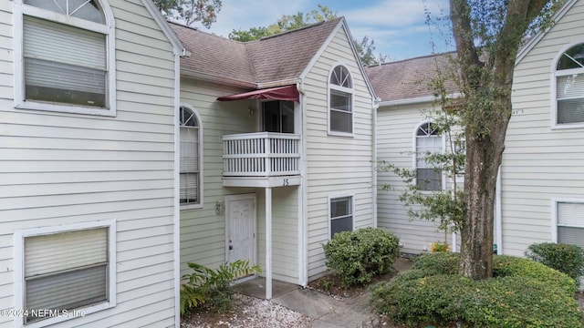 view of exterior entry featuring a shingled roof and a balcony