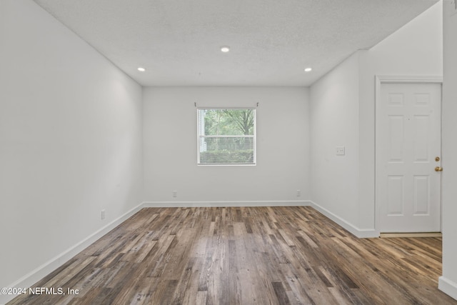 empty room featuring a textured ceiling, recessed lighting, wood finished floors, and baseboards