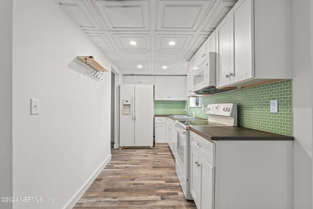 kitchen with white appliances, a sink, white cabinetry, backsplash, and dark countertops