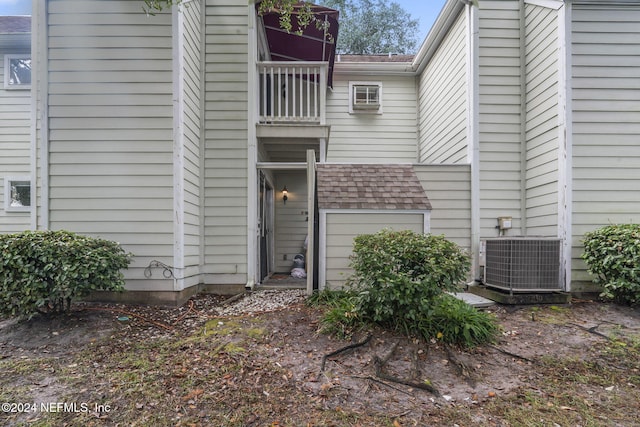 doorway to property with a balcony, a shingled roof, and central AC unit