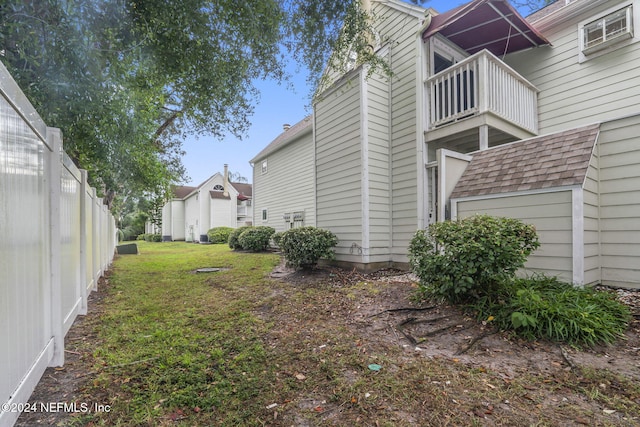 view of side of property featuring a shingled roof, a lawn, a balcony, and fence