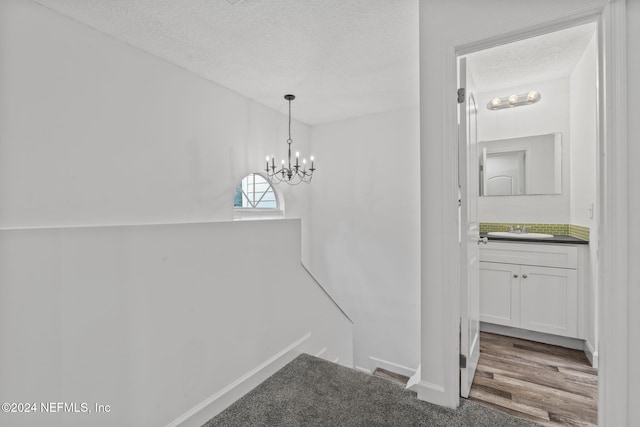 unfurnished dining area featuring a textured ceiling, a sink, wood finished floors, baseboards, and an inviting chandelier