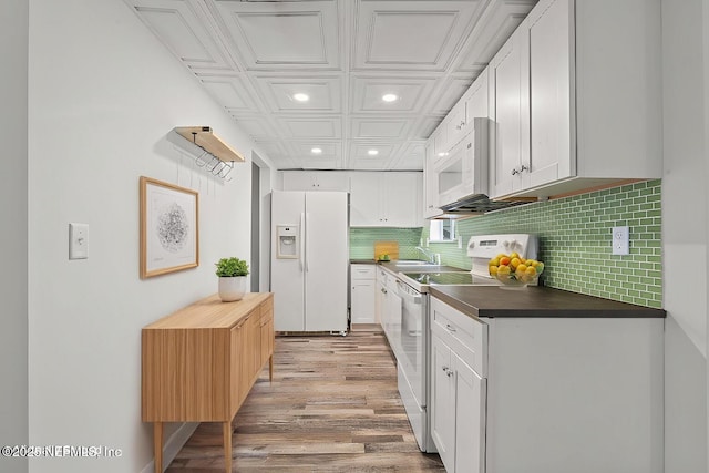 kitchen featuring tasteful backsplash, dark countertops, recessed lighting, white cabinetry, and white appliances