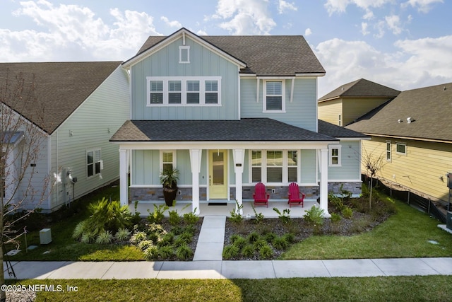 view of front of house featuring stone siding, a shingled roof, board and batten siding, and a front yard